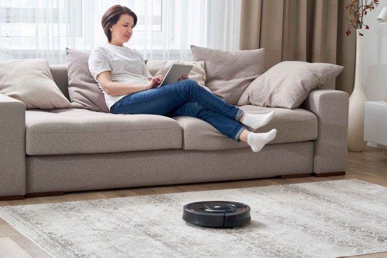 Robotic vacuum cleaner cleaning room while woman resting on sofa